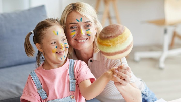 Smiling mother showing her daughter with down syndrome the model of the planet