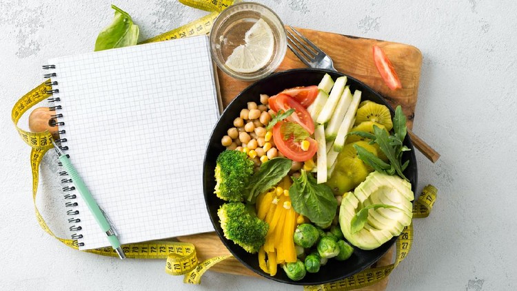 Ilustrasi Makanan Sehat Vegan healthy balanced diet concept. Vegetarian buddha bowl with blank notebook and measuring tape. hickpeas, broccoli, pepper, tomato, spinach, arugula and avocado in plate on white background. Top view