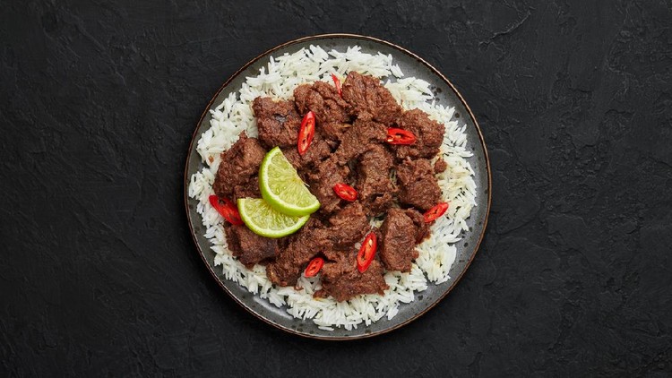 Beef Rendang on black plate at black slate table top. Indonesian padang cuisine meat dish. Asian food. Top view