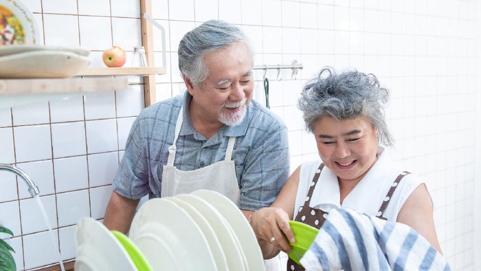 Happy asian elder senior couple washing dishes in sink at home in kitchen at home.