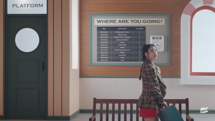 Di awal video, IU tampak memasuki sebuah stasiun kereta untuk melakukan perjalanan. Blazer motif plaid dan mini skirt merah membuat tampilannya terlihat cute. Dandanan rambut yang indah semakin melengkapinya. (Foto:youtube.com/1theK)