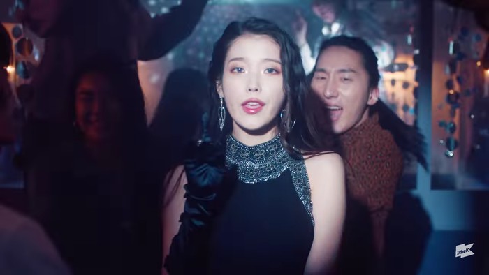 IU tampak elegan dengan sleeveless dress warna hitam di scene night party. Ia juga mengenakan kaos tangan hitam yang kece. Dengan rambut yang dibiarkan tergerai, pesona IU tampak sangat memukau. (Foto:youtube.com/1theK)