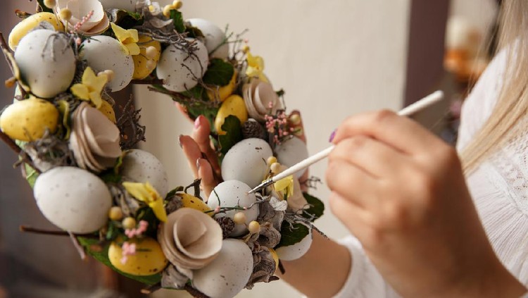 Girl paints on handmade wreath with Easter eggs. Woman draws on easter eggs