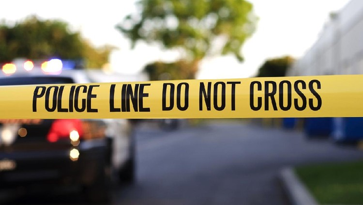 Ilustrasi garis polisi A blurred police car in the background behind yellow crime scene tape.
