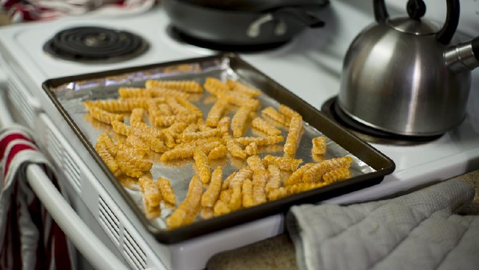 A baking sheet lined with foil, covered in frozen french fries, waiting to go in the oven