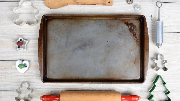 Overhead shot of a group of items for baking Christmas Cookies surrounding an empty cookie sheet. Horizontal format on a  rustic wood kitchen table.