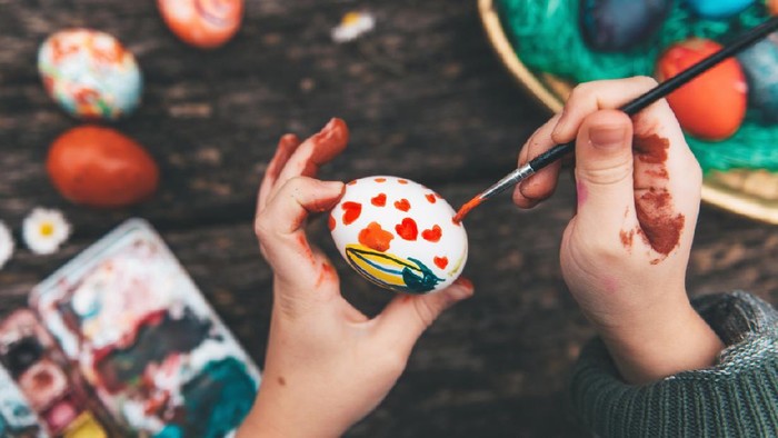 Overhead view on Childs hand painting easter eggs on old wooden table