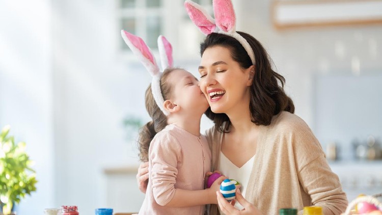 Happy holiday! A mother and her daughter are painting eggs. Family preparing for Easter. Cute little child girl is wearing bunny ears.
