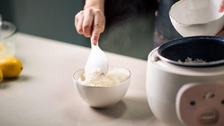 Woman taking out and serving fresh boiled fragrant jasmine rice from the rice cooker in the kitchen at home