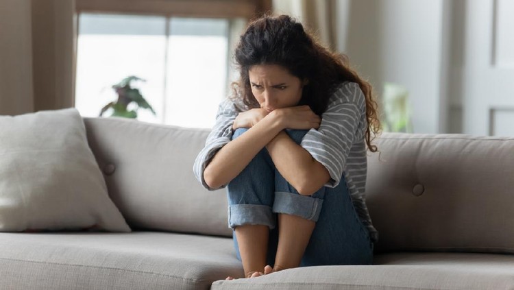 1207723232 Stressed young woman embracing knees, sitting alone on couch in living room, feeling depressed. Unhappy desperate millennial curly lady regretting of decision, thinking of personal problems at home.