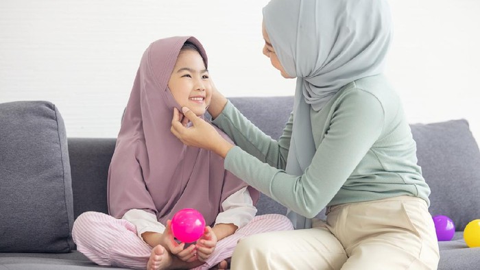 Portrait of happy lovely family arabic muslim mother and little muslim girls child with hijab dress smiling and having fun hugging and kissing together in living room