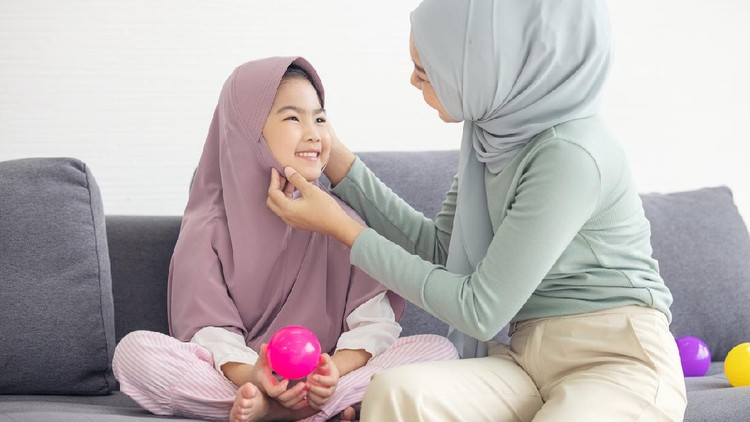 Portrait of happy lovely family arabic muslim mother and little muslim girls child with hijab dress smiling and having fun hugging and kissing together in living room