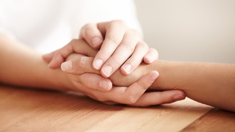 Hands holding one another on a table in prayer