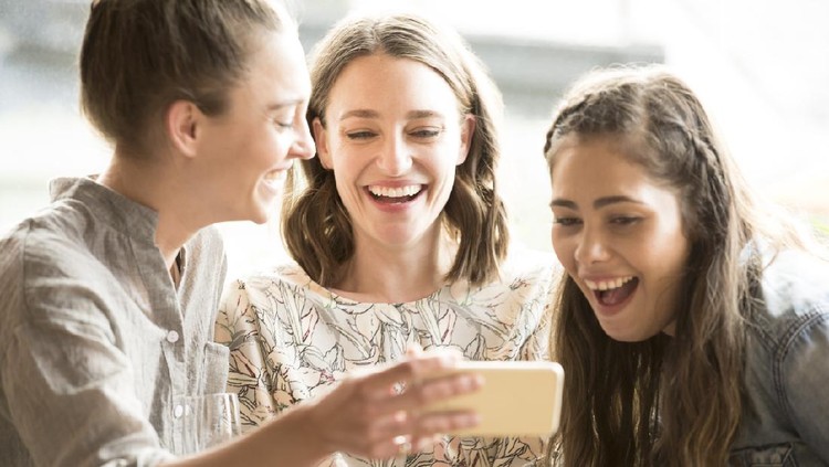 Three women looking at smartphone, smiling and laughing. Three female friends using social media, having fun, togetherness