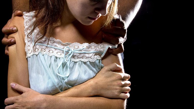 Oppressive man behind a female victim.  The image depicts domestic violence, an abusive relationship, or a obsessive controlling partner.  The identities of the models are obscured.  This is an illustrative editorial and not real.  The man is clutching the woman who looks victimized.
