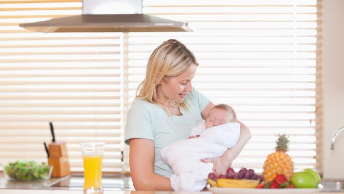 Young woman holding her sleeping baby in the kitchen