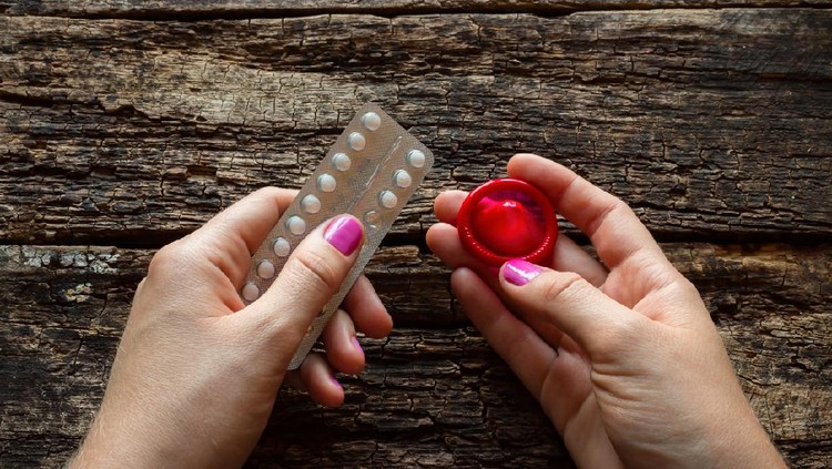 young woman holding a birth control pills and a condom