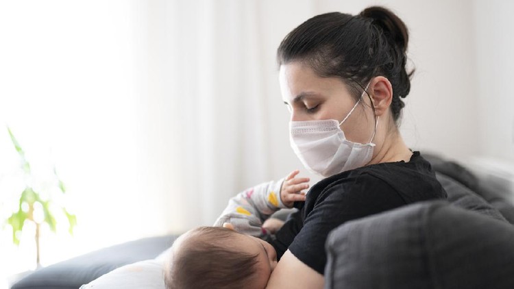 Mother with mask breastfeeding her little baby