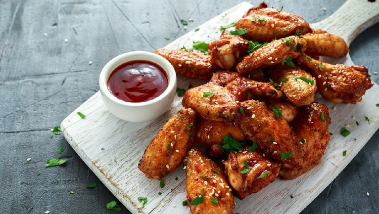 Baked chicken wings with sesame seeds and sweet chili sauce on white wooden board