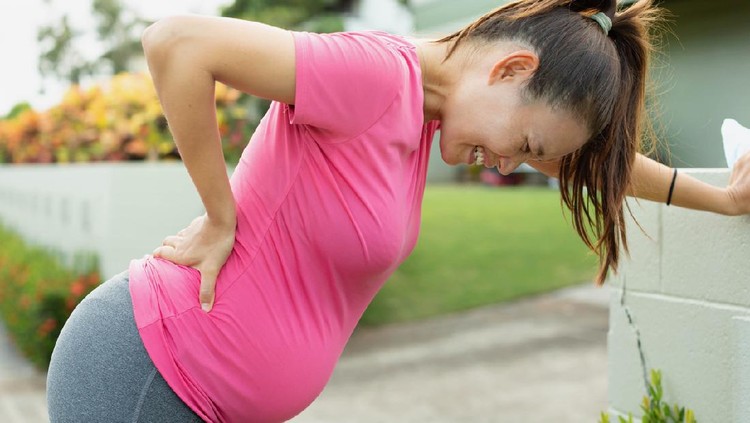 hamil A pregnant mom with a big belly stopping to rest from exercising, bending down from a painful cramp and back unjury.
