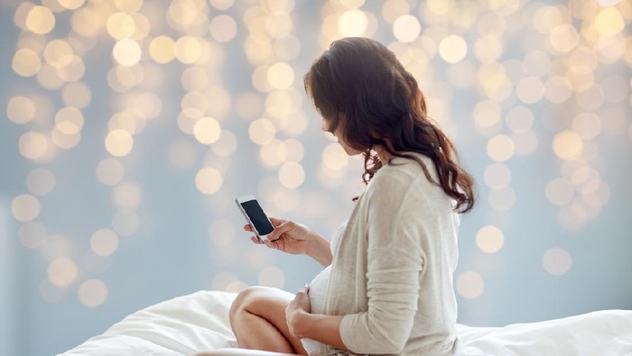 Beautiful young pregnant woman listening to music and sitting on sofa at living room. Relax, rest time concept.