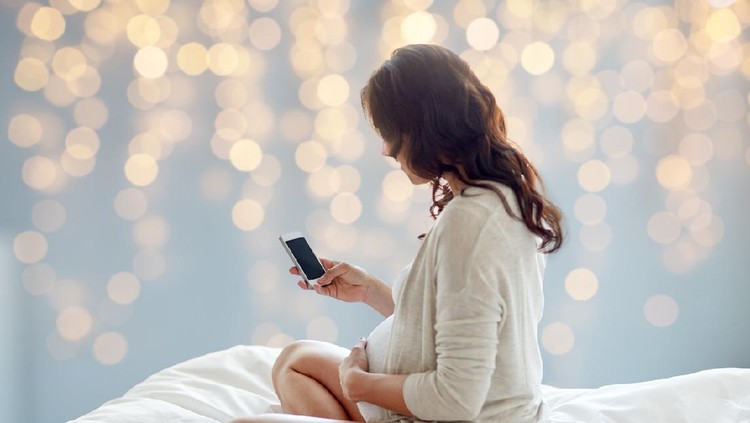 Beautiful young pregnant woman listening to music and sitting on sofa at living room. Relax, rest time concept.