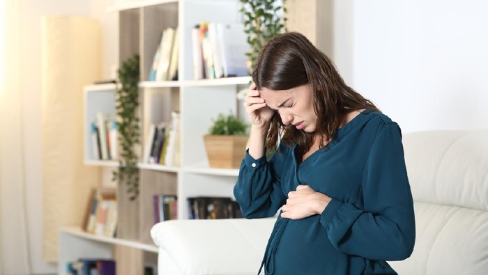 A pregnant mom with a big belly stopping to rest from exercising, bending down from a painful cramp and back unjury.