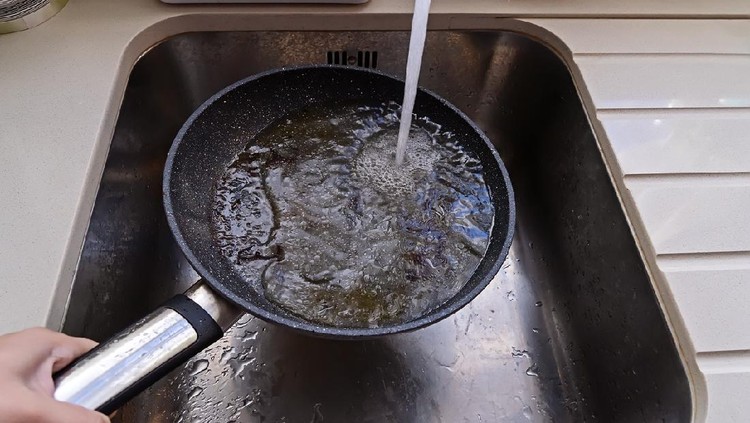POV of frying pan with non-stick surface and hot oil under water tap flow in sink. Care kitchenware concept