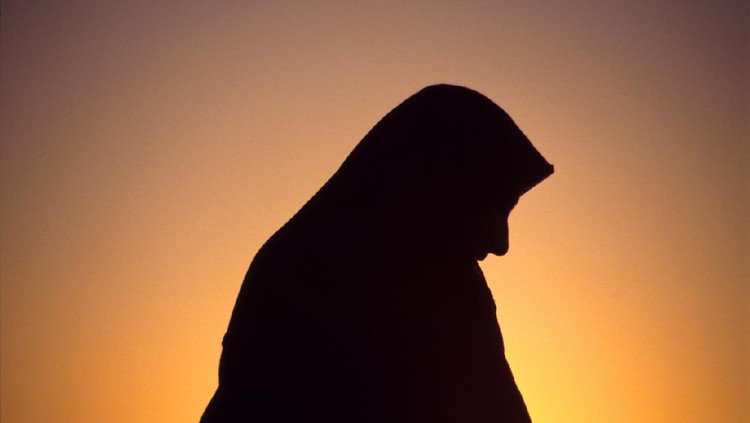 Arab woman with veil against orange yellow sky