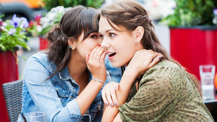 Two female friends sitting in a sidewalk cafe. They are whispering and gossiping.