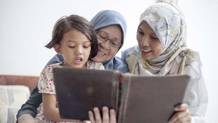 Two Malay woman reading to a young girl using a tablet that looks like a book