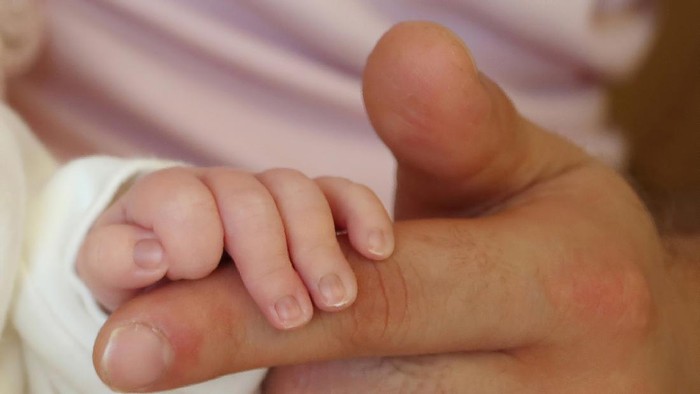 A newborn baby holding his father's hand