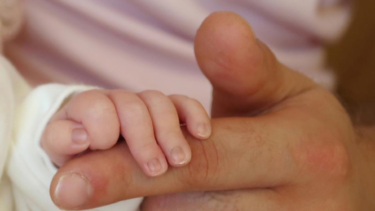A newborn baby holding his father's hand
