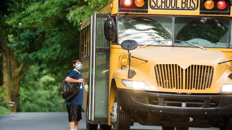 bus sekolah Young female bus driver driving he school bus, wearing a face mask. She is taking care that kids sit down.
