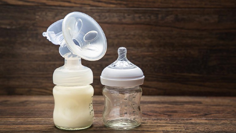 Baby bottle with breast pump attachement and empty bottle against a wood background