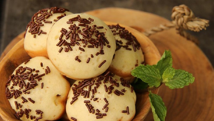 Kue Cubit, a popular street food and snack from Betawi, Jakarta. It is the Indonesian version of Dutch's poffertjes; with added topping of chocolate sprinkles instead of powder sugar. The kue cubit are arranged on a natural wooden bowl. A wooden block is used as the base; which then placed on a metal baking sheet.