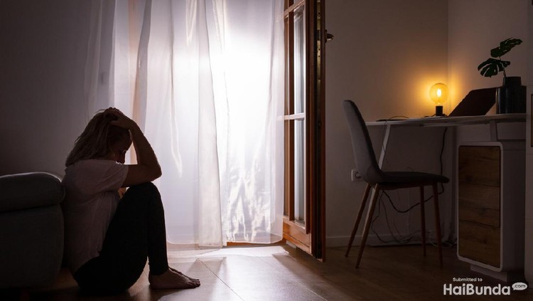 Side view full length shot of a sad depressed woman sitting on the floor and crying at home