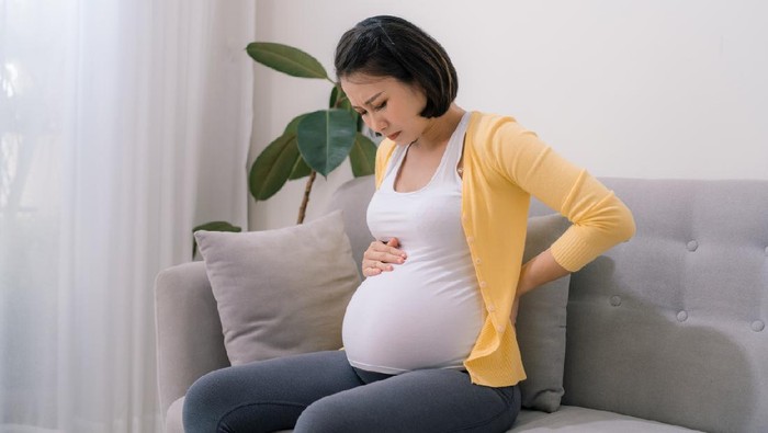 Asian pregnant woman has backache and feel depressed sitting on the couch