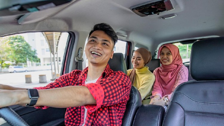 Three friend in the car. The driver is a male and looking to rear seat at mirror and smiling. The passenger is two asian hijab women smiling and laughing in the car