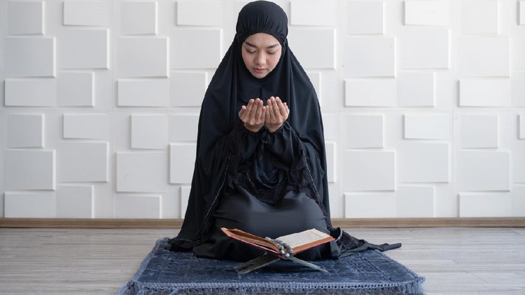 Muslim woman pray on hijab praying with Koran on mat indoors