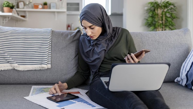 Focused Young Muslim Female Entrepreneur Wearing a Hijab Reading Through Paperwork While Working in Her Home Office. Work Opportunities For Muslim Women Concept. Freelance Concept.