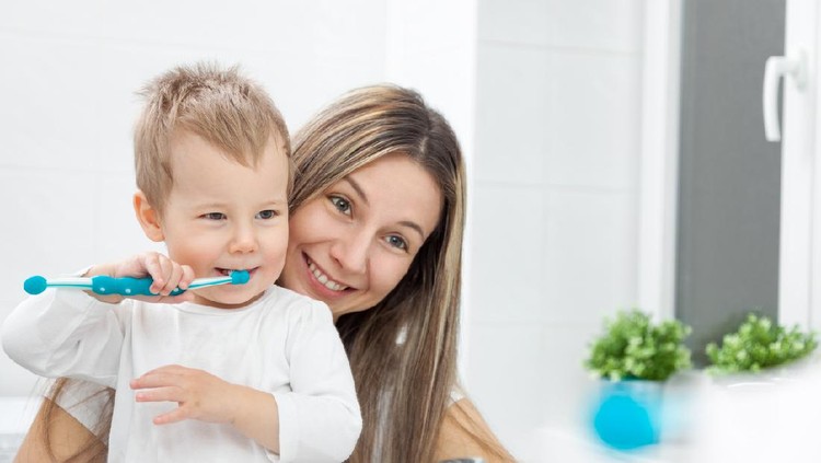 Mom brushes baby's teeth with a silicone brush that fits on her finger
