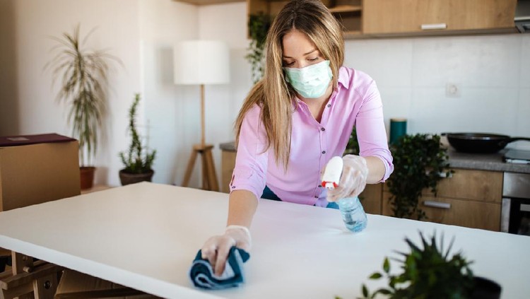 Young woman wearing mask for protection of COVID-19 pandemic while disinfecting her new house