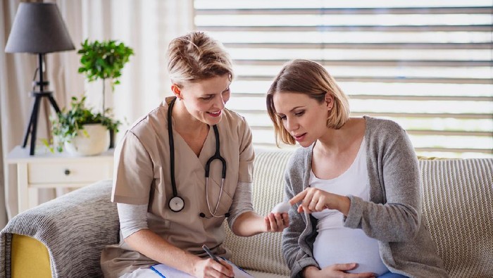 A healthcare worker examining pregnant woman indoors at home, checking sugar level.