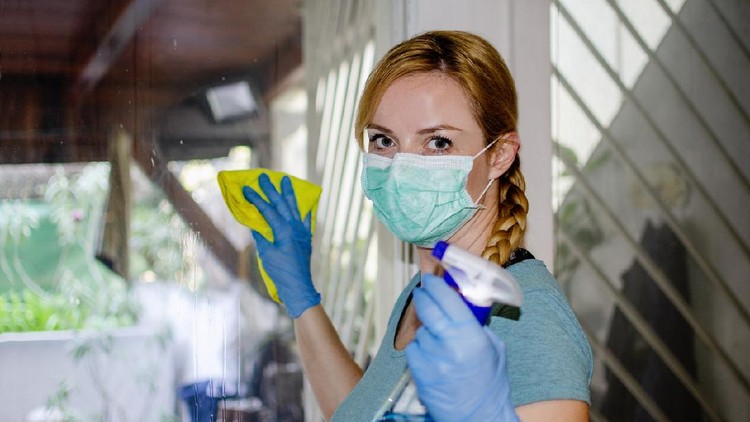 Woman with protective mask and latex gloves desinfecting the window glass at home.Respiratory system Protection from cleaning sanitary products chemicals