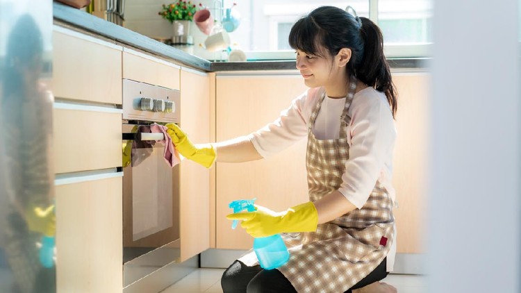 Asian woman wearing rubber protective gloves cleaning oven in her home during Staying at home using free time about their daily housekeeping routine.
