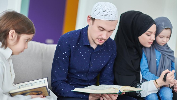 Young muslim family reading Quran during Ramadan. Parents and kids worshiping to God, in islamic clothes at modern home