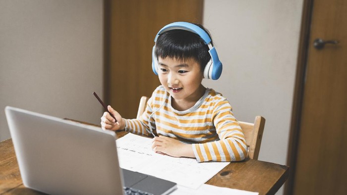 Asian boy attending online classroom at home.