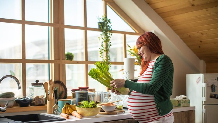hamil Pregnant redhead woman preparing healthy salad in bright kitchen