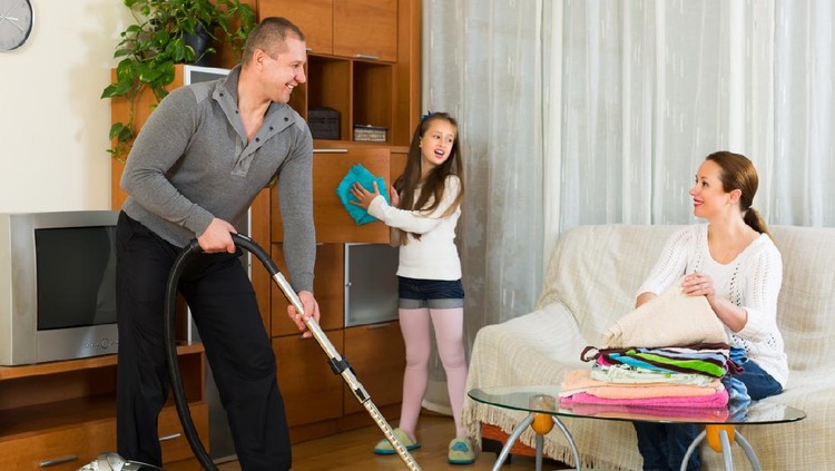 Little girl helping happy parents to clean at living room. Focus on man